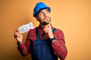Young builder man wearing safety helmet offering help and support over yellow background serious...