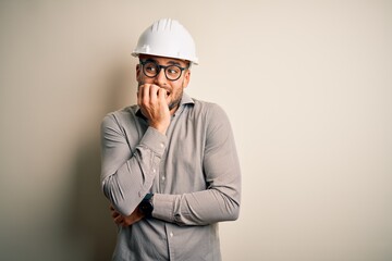 Young architect man wearing builder safety helmet over isolated background looking stressed and nervous with hands on mouth biting nails. Anxiety problem.