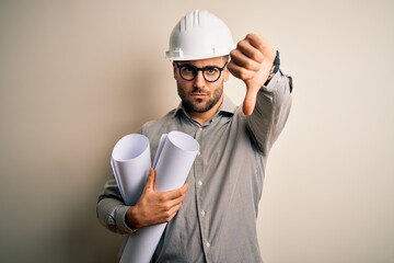 Young architect man wearing contractor helmet holding project paper plan over isolated background...