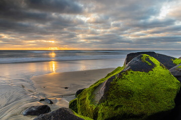 The setting sun brightens mossy boulders on the beach at Carlsbad, CA.