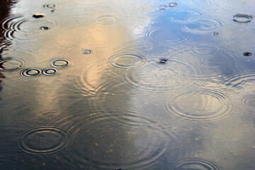 Drops of rain bubbling in a puddle with the reflection of light