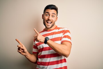 Young handsome man wearing casual striped t-shirt standing over isolated white background smiling and looking at the camera pointing with two hands and fingers to the side.