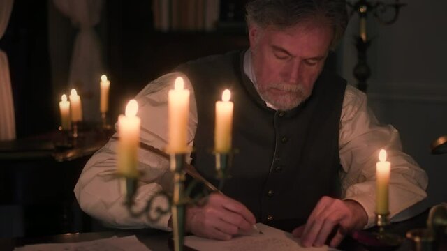 Scene moves from an older gentleman of the 18th century lit by candlelight down to a letter he is composing using a quill pen and ink from a fancy ink well.