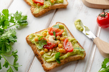 Vegan sandwich with avocado, nuts, vegetables and olive oil on white wooden table