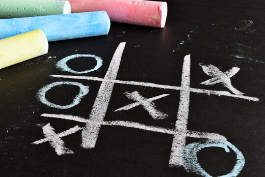 A close up image of a tic-tac-toe game done in brightly colored chalk on a black background. 