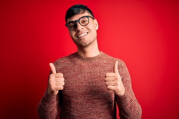 Young handsome hispanic man wearing nerd glasses over red background success sign doing positive...