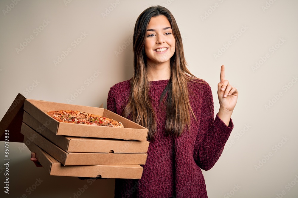 Sticker young beautiful girl holding delivery boxes with italian pizza standing over white background surpri