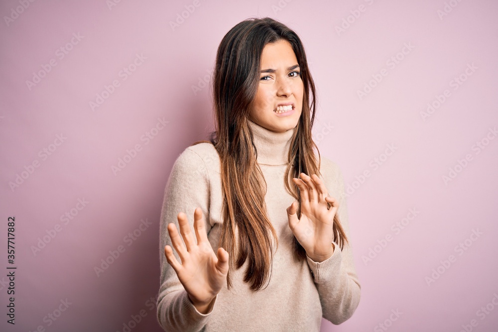 Poster Young beautiful girl wearing casual turtleneck sweater standing over isolated pink background disgusted expression, displeased and fearful doing disgust face because aversion reaction.