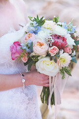 bride at a wedding holding a floral bouquet of flowers in  colors of pink, peach, blue and white