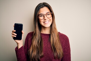 Young beautiful girl wearing glasses showing smartphone over isolated white background with a happy...