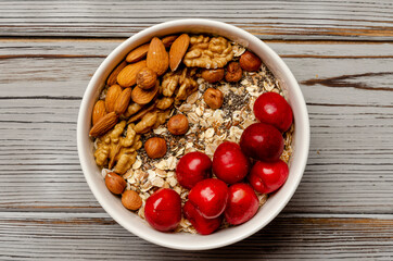 bowl of oat granola with freshberries and nuts on white wooden board for healthy