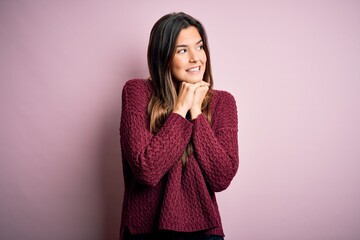 Young beautiful girl wearing casual sweater over isolated pink background laughing nervous and excited with hands on chin looking to the side