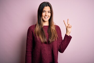 Young beautiful girl wearing casual sweater over isolated pink background showing and pointing up with fingers number two while smiling confident and happy.