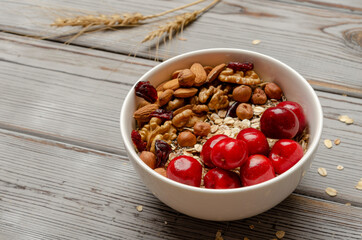 bowl of oat granola with freshberries and nuts on white wooden board for healthy