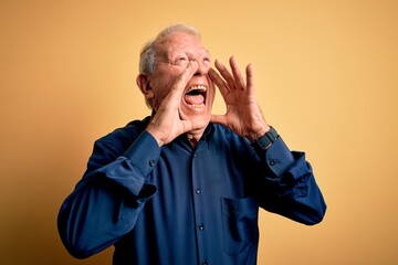 Grey haired senior man wearing casual blue shirt standing over yellow background Shouting angry out...