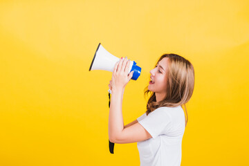 Fototapeta premium Asian Thai happy portrait beautiful cute young woman stand to make announcement message shouting screaming in megaphone looking to side away, studio shot isolated on yellow background with copy space