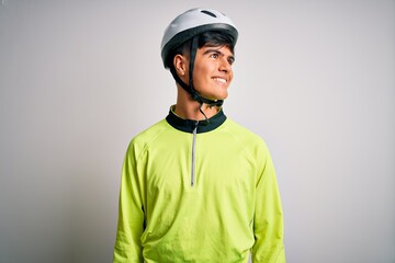 Young handsome cyclist man wearing security bike helmet over isolated white background looking away to side with smile on face, natural expression. Laughing confident.