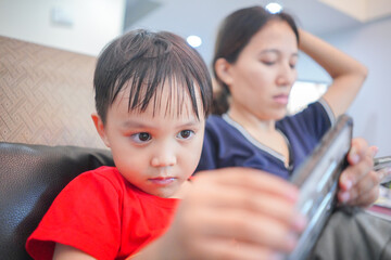 portrait of little asian boy sitting with mother watching smartphone 