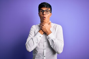 Young handsome business man wearing shirt and glasses over isolated purple background shouting and suffocate because painful strangle. Health problem. Asphyxiate and suicide concept.
