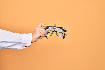 Hand of caucasian young woman holding optometry glasses over isolated yellow background