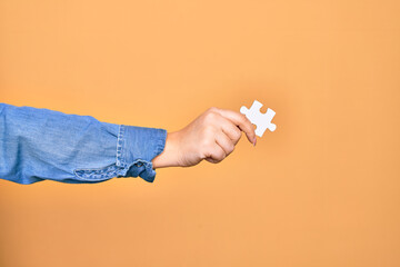 Hand of caucasian young woman holding piece of puzzle over isolated yellow background