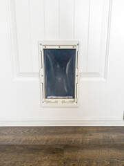Fototapeta na wymiar Close up of pet door or pet flap against white wooden panelled door of home