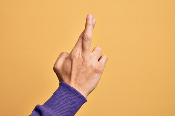 Hand of caucasian young man showing fingers over isolated yellow background gesturing fingers crossed, superstition and lucky gesture, lucky and hope expression