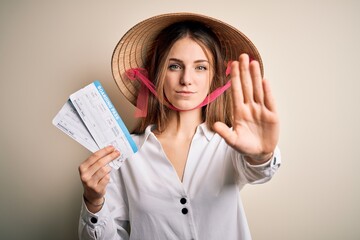 Young beautiful redhead tourist woman wearing asian traditional hat holding boarding pass with open hand doing stop sign with serious and confident expression, defense gesture