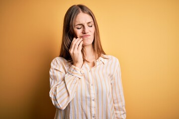 Young beautiful redhead woman wearing casual striped shirt over isolated yellow background touching mouth with hand with painful expression because of toothache or dental illness on teeth. Dentist