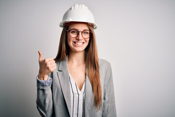 Young beautiful redhead architect woman wearing security helmet over white background doing happy...