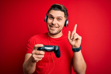 Young gamer man with blue eyes playing video games using gamepad joystick surprised with an idea or question pointing finger with happy face, number one © Krakenimages.com