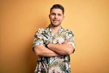 Young man with blue eyes on vacation wearing floral summer shirt over yellow background happy face...