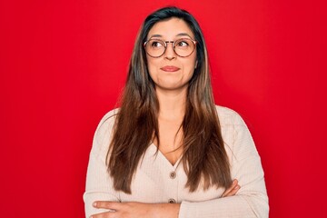 Young hispanic smart woman wearing glasses standing over red isolated background smiling looking to the side and staring away thinking.