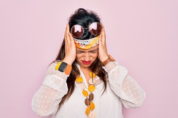 Young hispanic hippie woman wearing fashion boho style and sunglasses over pink background suffering from headache desperate and stressed because pain and migraine. Hands on head.