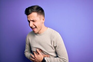 Obraz premium Young handsome caucasian man wearing casual sweater over purple isolated background with hand on stomach because nausea, painful disease feeling unwell. Ache concept.
