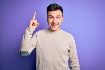 Young handsome caucasian man wearing casual sweater over purple isolated background pointing finger up with successful idea. Exited and happy. Number one.