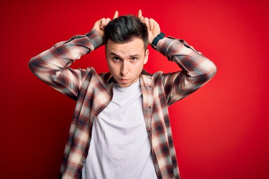 Young handsome caucasian man wearing casual modern shirt over red isolated background doing funny gesture with finger over head as bull horns