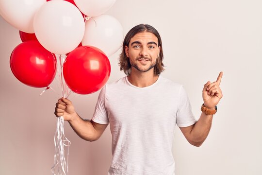 Young handsome man holding balloons smiling happy pointing with hand and finger to the side