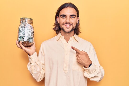 Young handsome man holding jar with savings smiling happy pointing with hand and finger