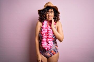 Young beautiful arab woman on vacation wearing swimsuit and hawaiian lei flowers touching mouth with hand with painful expression because of toothache or dental illness on teeth. Dentist