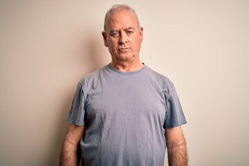 Middle age handsome hoary man wearing t-shirt standing over isolated white background with serious...