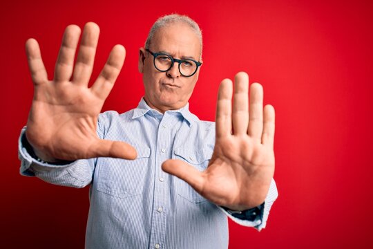 Middle age handsome hoary man wearing casual striped shirt and glasses over red background doing frame using hands palms and fingers, camera perspective