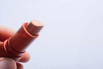 Closeup shot of a person holding a beige lipstick isolated on a grey background