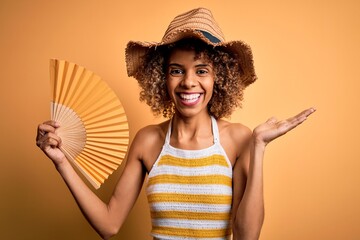 African american tourist woman with curly on vacation wearing summer hat using hand fan very happy and excited, winner expression celebrating victory screaming with big smile and raised hands