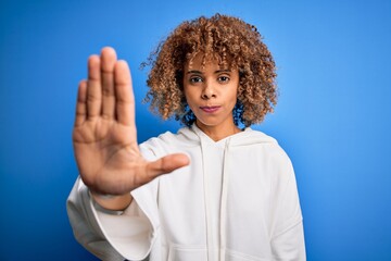 Beautiful african american sporty woman wearing casual sweatshirt over blue background doing stop sing with palm of the hand. Warning expression with negative and serious gesture on the face.