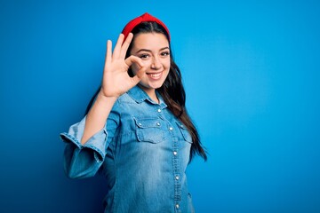 Young brunette woman wearing casual denim shirt over blue isolated background smiling positive doing ok sign with hand and fingers. Successful expression.