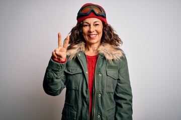 Middle age skier woman wearing snow sportswear and ski goggles over white background showing and pointing up with fingers number two while smiling confident and happy.