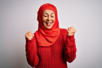 Middle age brunette woman wearing muslim traditional hijab over isolated white background very happy and excited doing winner gesture with arms raised, smiling and screaming for success. Celebration