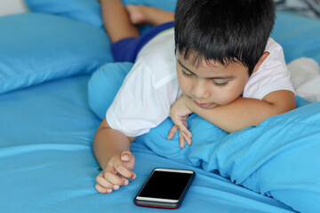 Cute asian boy playing games on smartphone. Child using a smartphone while lying on the bed. Social and technology concept.