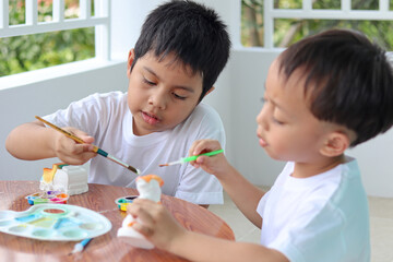 Cute little boys painting Plaster doll at the table with art supplies.